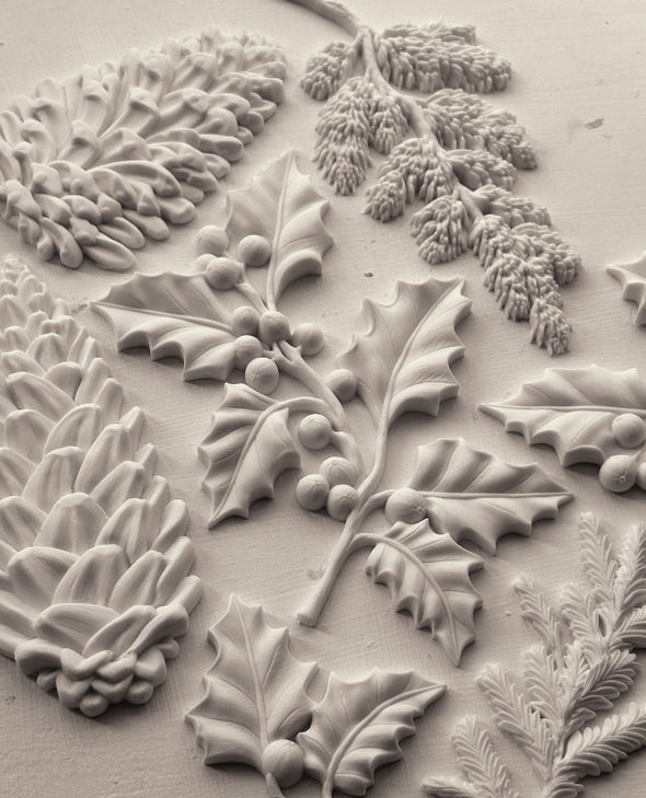 Styled castings from the IOD Winter Forage Mould showing pinecones, holly, and winter botanicals.