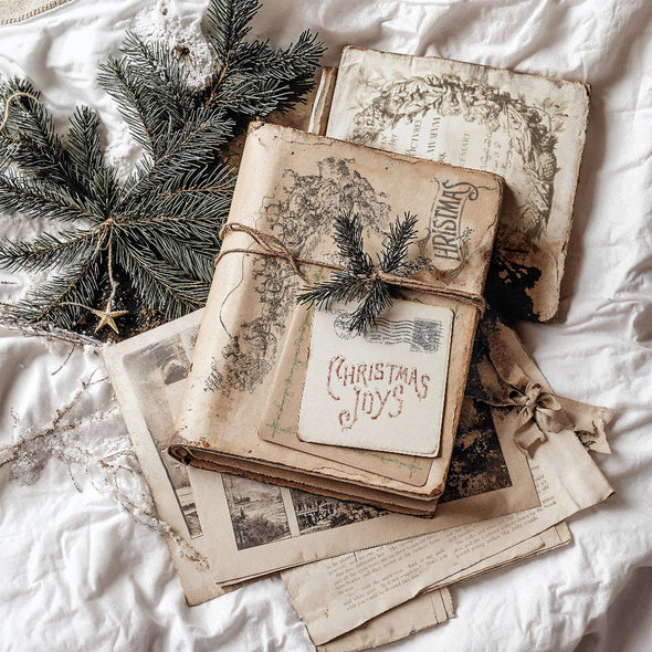 Styled flat lay of IOD Christmas Post Stamp impressions on vintage papers with holiday greenery.